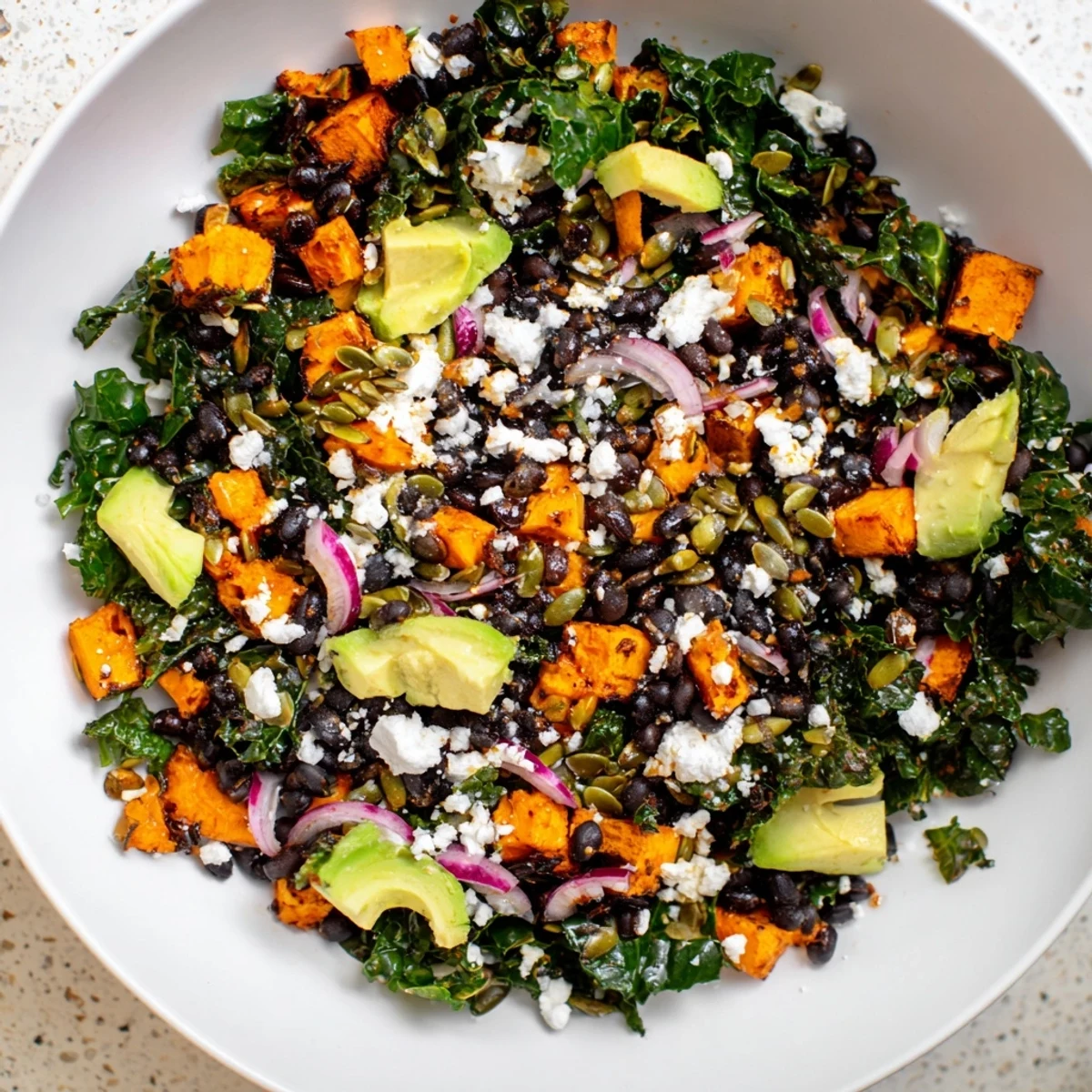 Tender massaged kale salad with sweet potato, black beans, and a creamy lime dressing is pictured.