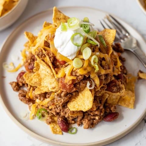 Mouthwatering Chili Cheese Frito Pie garnished with sour cream and green onions, served warm.  