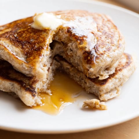 A plate of fluffy banana oat pancakes, drizzled with maple syrup, looking warm and inviting.