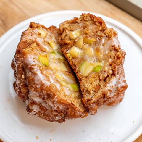 A close-up of fluffy, warm homemade apple fritters, with visible apple pieces and a sweet, shiny glaze.
