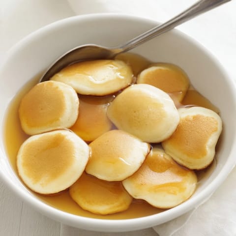 Tiny, perfectly cooked Fluffy Pancake Cereal pieces with maple syrup and milk, breakfast bliss.