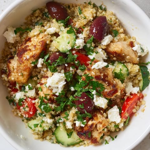 Golden seared chicken tops a colorful Mediterranean Chicken Bowl filled with chickpeas, tomatoes, and red onion, garnished with fresh parsley and tangy feta.
