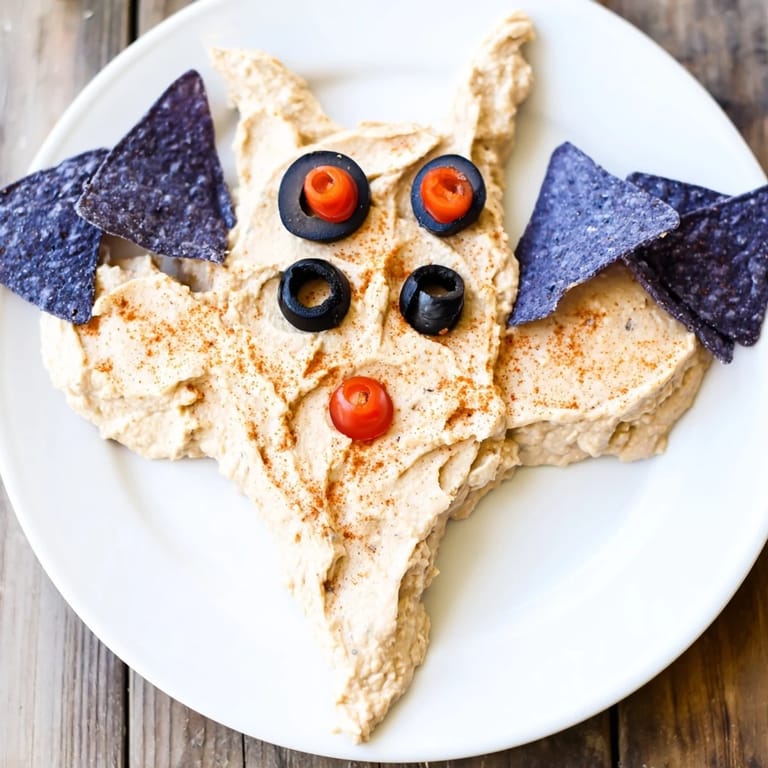 Halloween Spooky Bat Bean Dip Platter on a platter encircled by crunchy tortilla chips and fresh vegetable sticks.