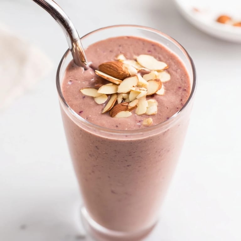In a bright kitchen, a creamy Cherry Almond Smoothie pours from a blender into a glass, showing off its rich red hue.